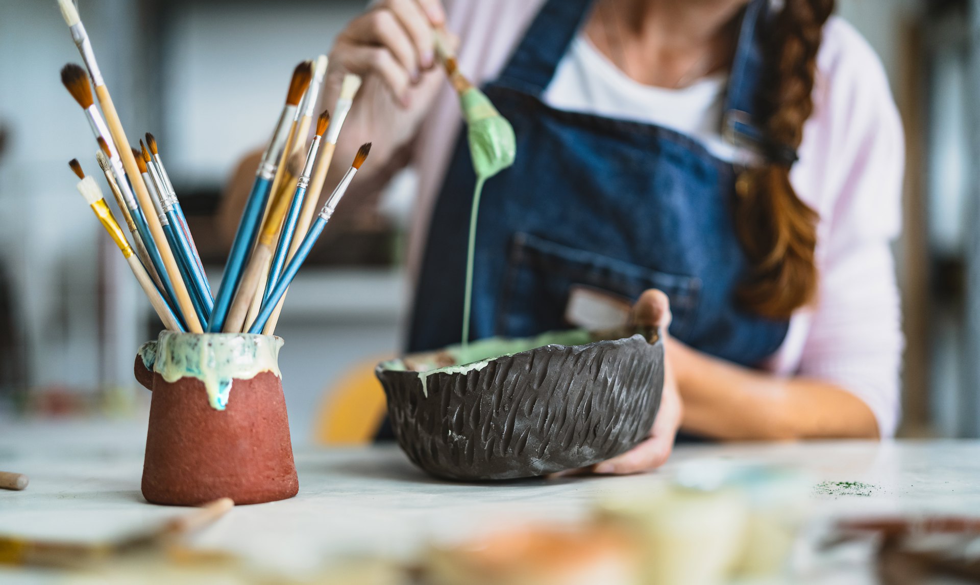 Woman mixing paint with brush inside ceramic bowl in workshop studio - Artisan work and creative craft concept